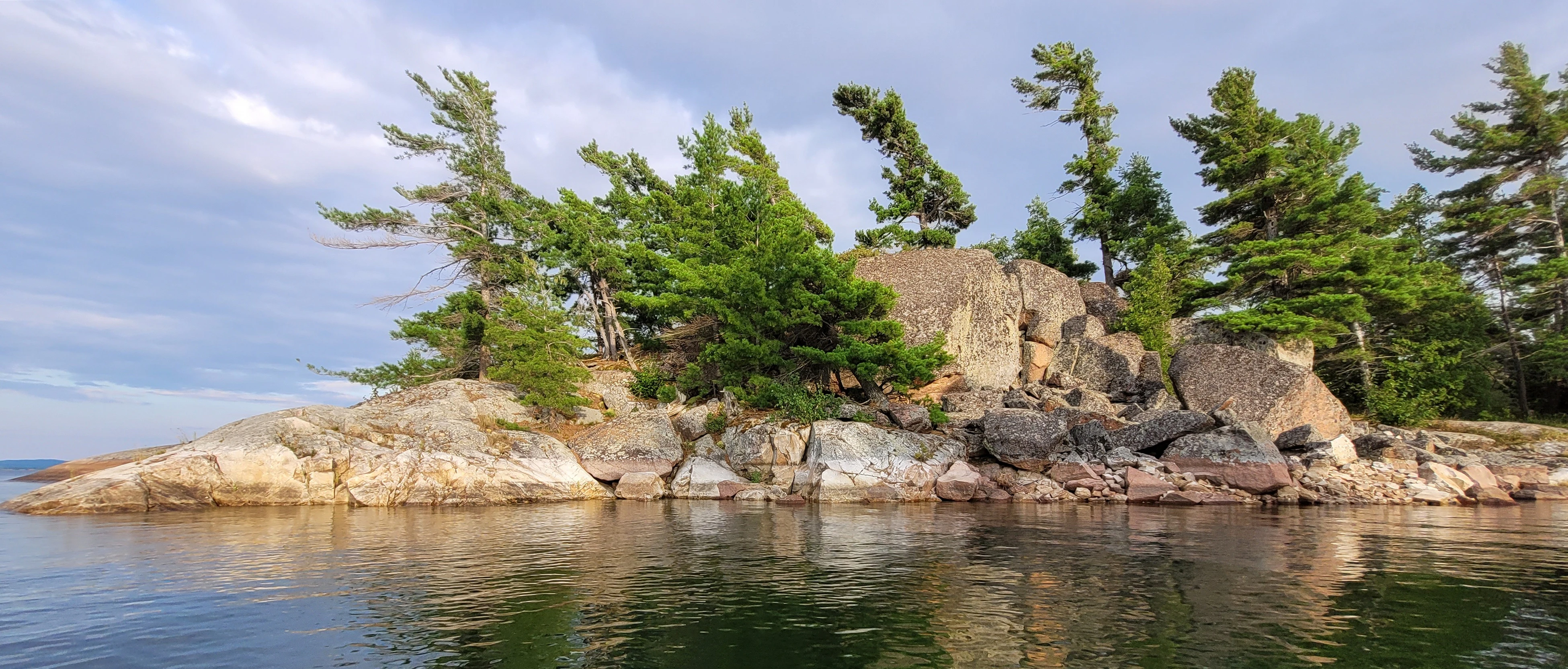A calm cove cliff edge with rocks and trees reflecting off the calm water on North Benjamin Island in The North Channel of Lake Huron